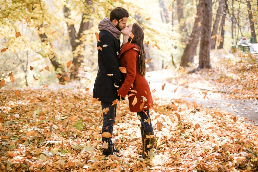 Romantic photo of cute couple outdoors in fall. Young man and woman kissing in falling leaves