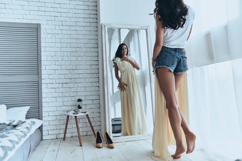 Fits perfectly! Rear view of attractive young woman trying on her dress while looking in the mirror at home