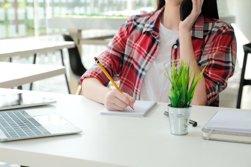 woman girl teenager freelancer talking on phone writing note at workplace