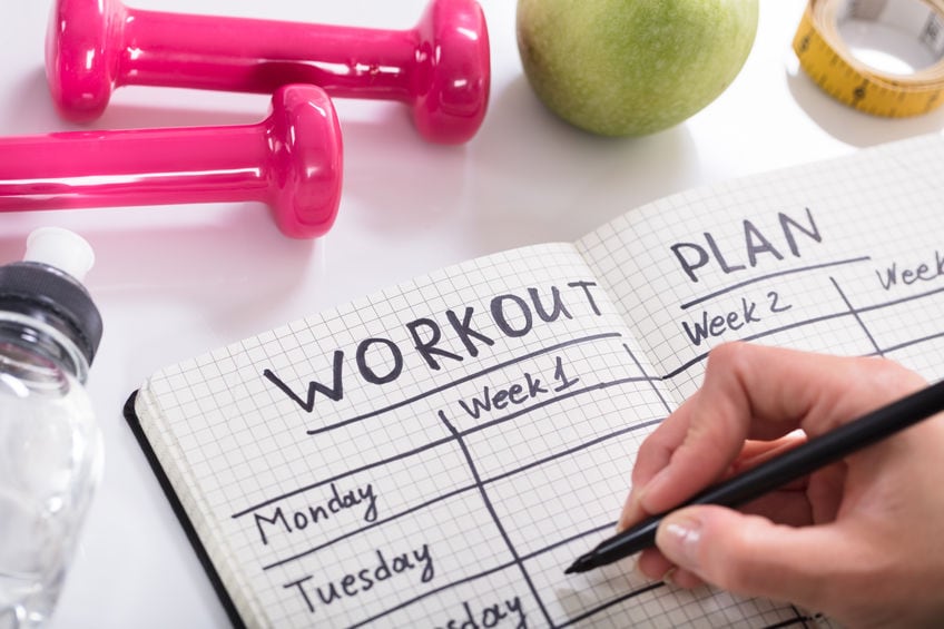 Woman Writing Workout Plan In Notebook At Wooden Desk