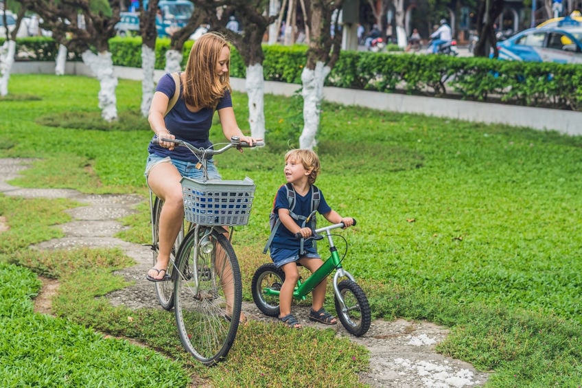 Happy family is riding bikes outdoors and smiling. Mom on a bike and son on a balancebike.