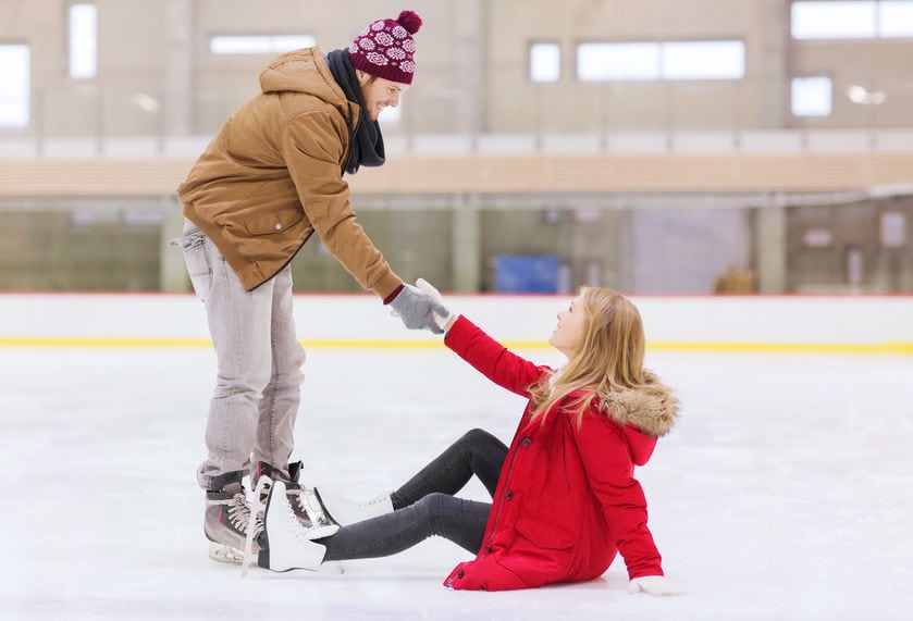 people, friendship, sport and leisure concept - smiling man helping women to rise up on skating rink