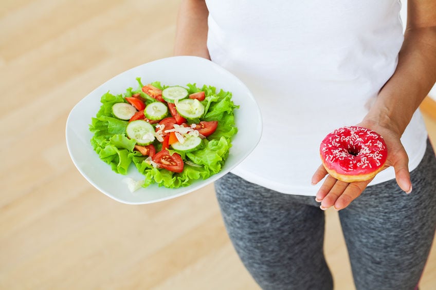 Diet concept, woman measures weight on electronic scales while holding calorie donut.